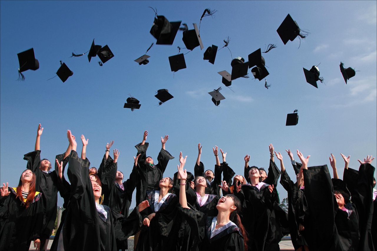 ours-journey Group of graduates celebrating by throwing caps in the air during a sunny day.