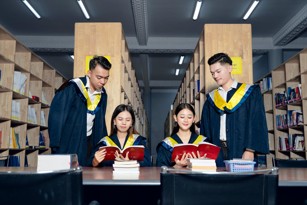 contact-img A group of university graduates in academic gowns study together in a library.
