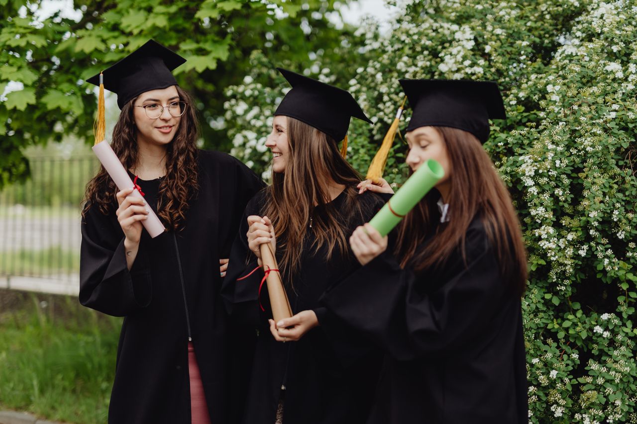 Mastering the First Impression: Your intriguing post title goes here Three women in graduation gowns and caps celebrating their achievement with diplomas in an outdoor setting.